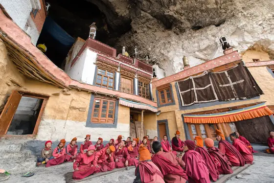 Monks gathered below a monastery built into the rock face
