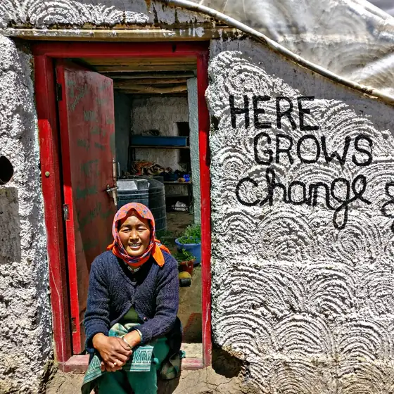 Changpa woman seated in a red doorway outside a high-altitude homestead