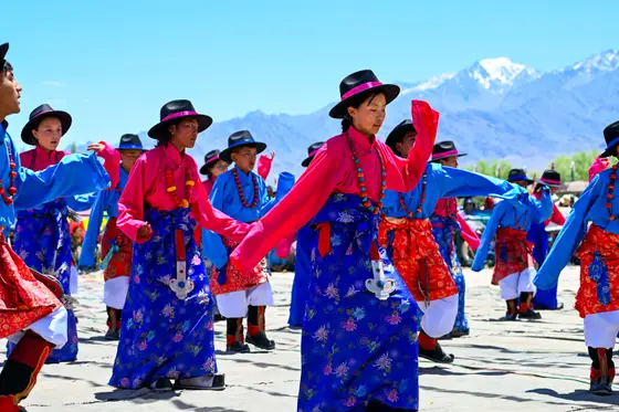 Festival dancers in traditional dress beneath snowy peaks