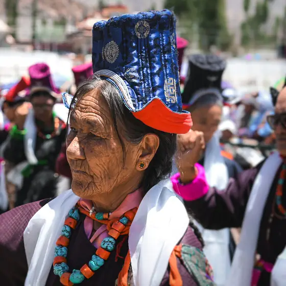 Elder in a blue ceremonial headdress during a Ladakhi festival gathering