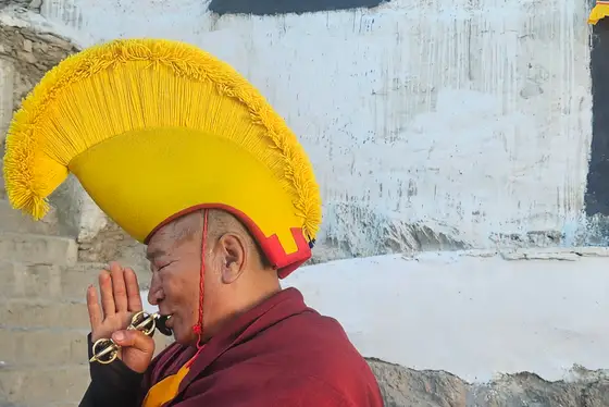 Monk in ceremonial yellow hat beside a whitewashed monastery wall