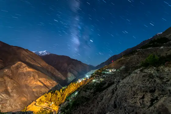 Star-filled night sky above a lit mountain village in Ladakh