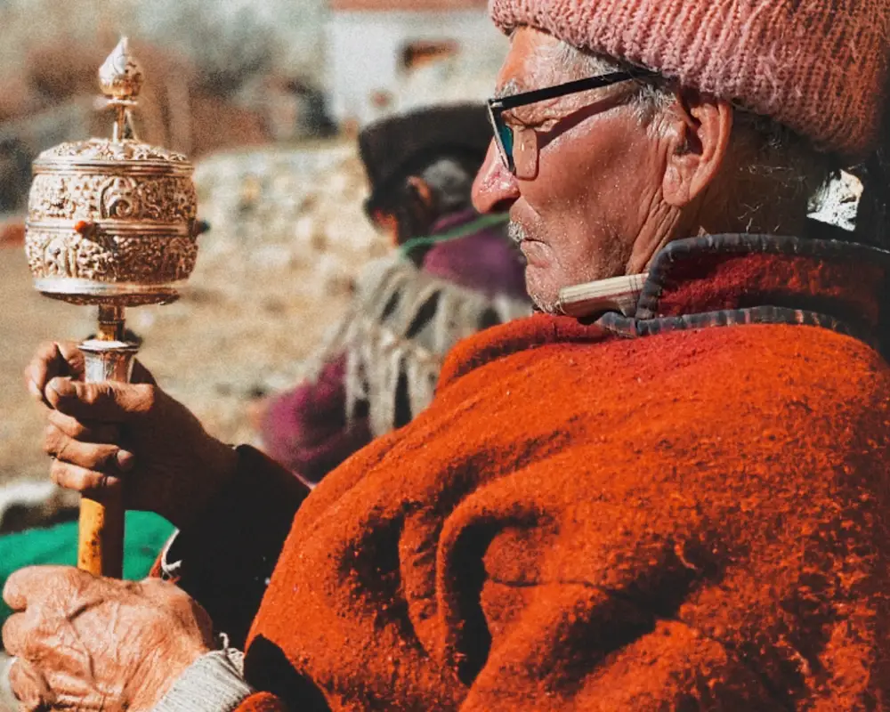 Older Ladakhi man holding a prayer wheel